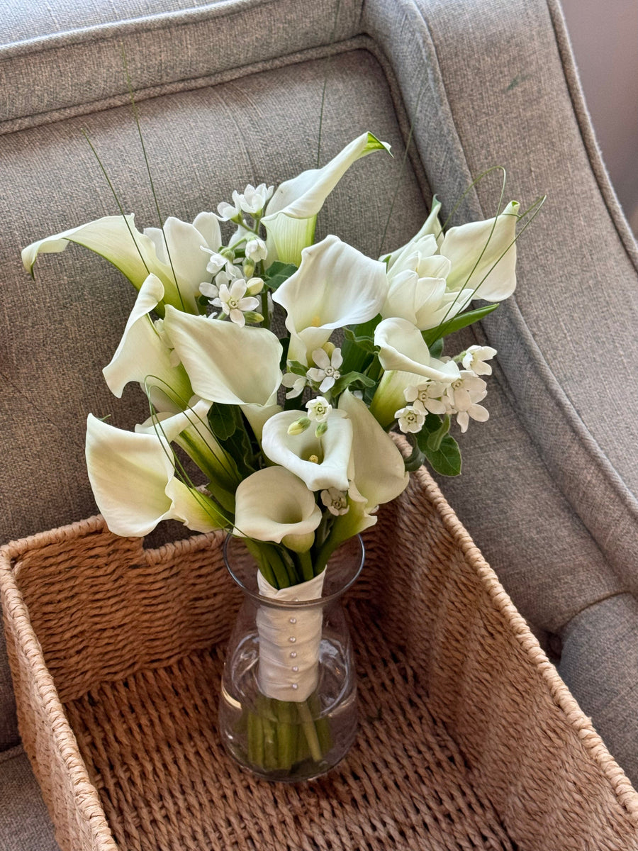 Bouquet of white flowers in a clear vase on a woven basket with a gray sofa background