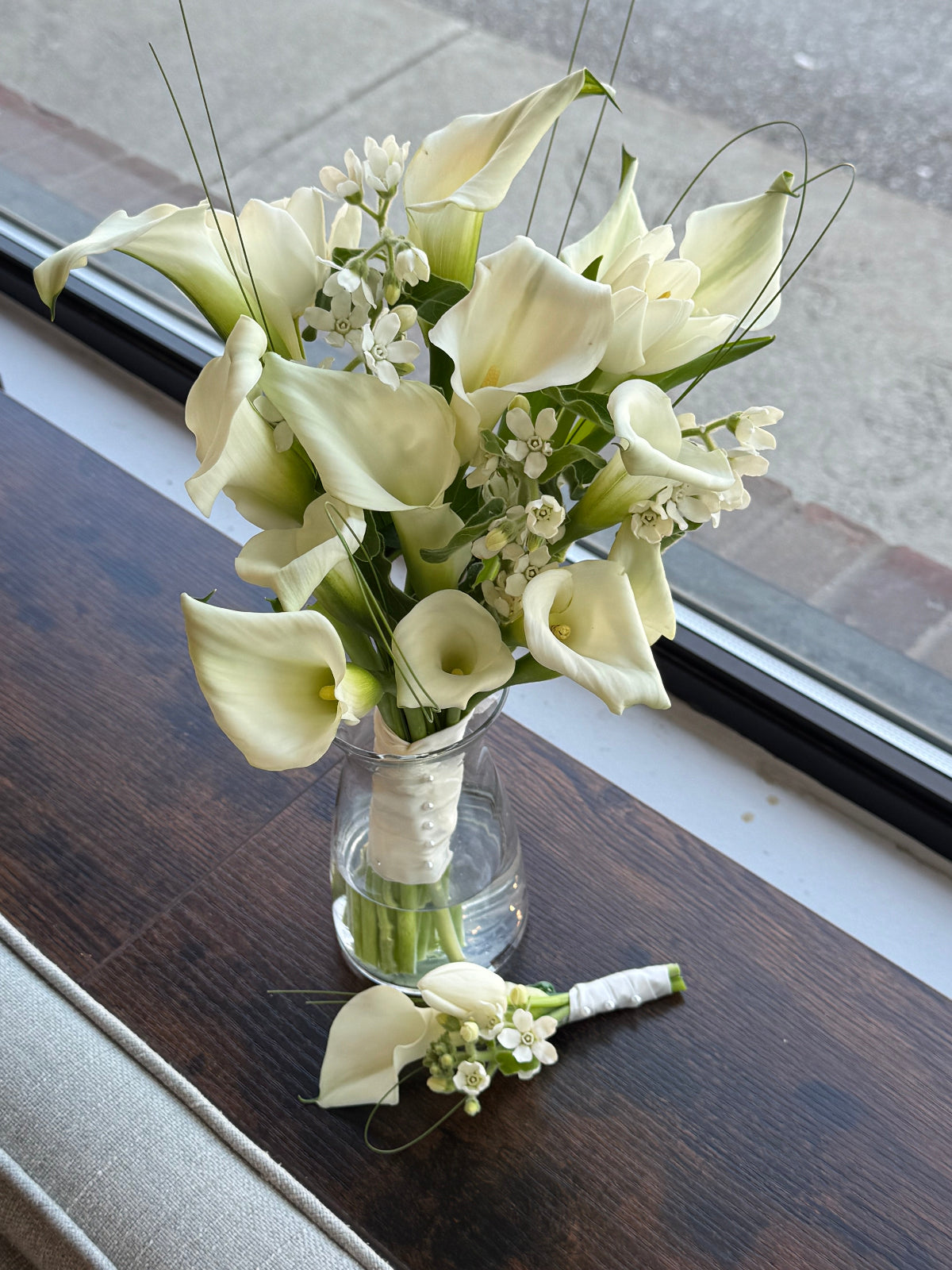 Bouquet and boutonniere of white flowers on a wooden surface.