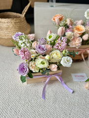 flowers in a wooden box with a ribbon on a textured surface.
