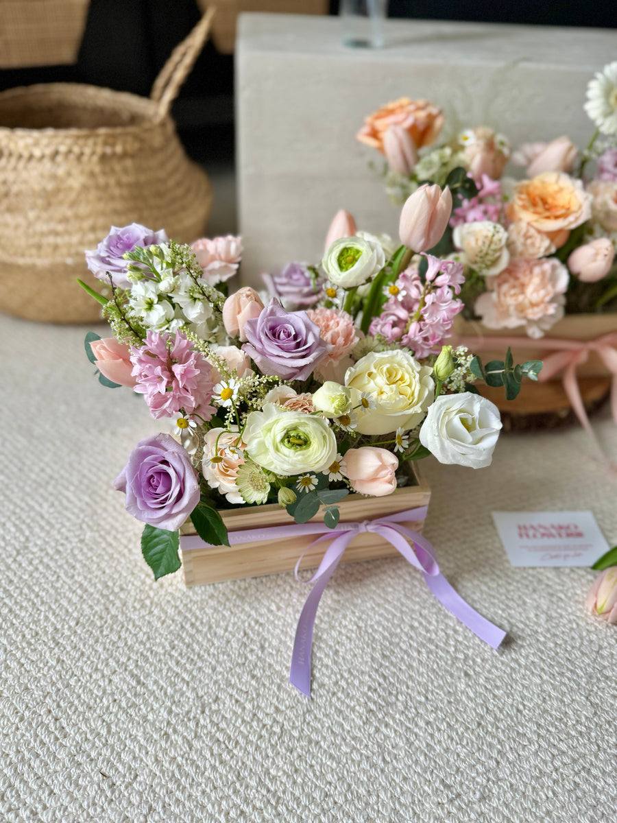 flowers in a wooden box with a ribbon on a textured surface.
