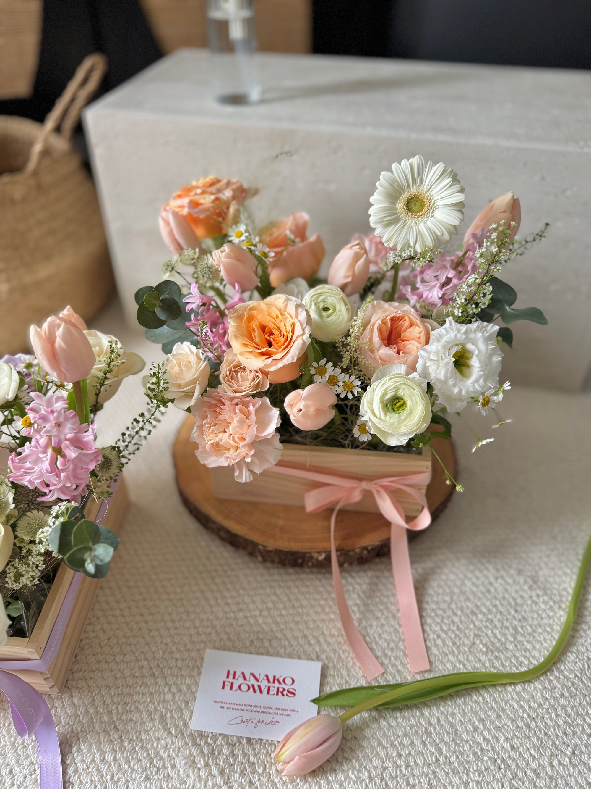 floral arrangement with a pink ribbon on a textured surface, featuring the brand 'Hanako Flowers'.