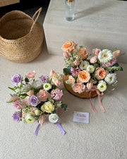Two floral arrangements on a textured surface with a woven basket in the background.