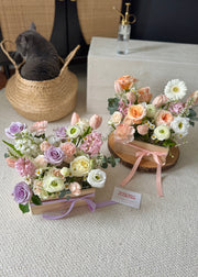 Fresh flower arrangements in wooden box with a cat in the background.