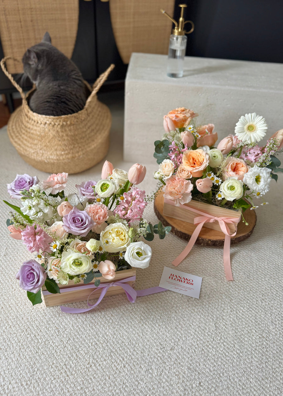 Fresh flower arrangements in wooden box with a cat in the background.