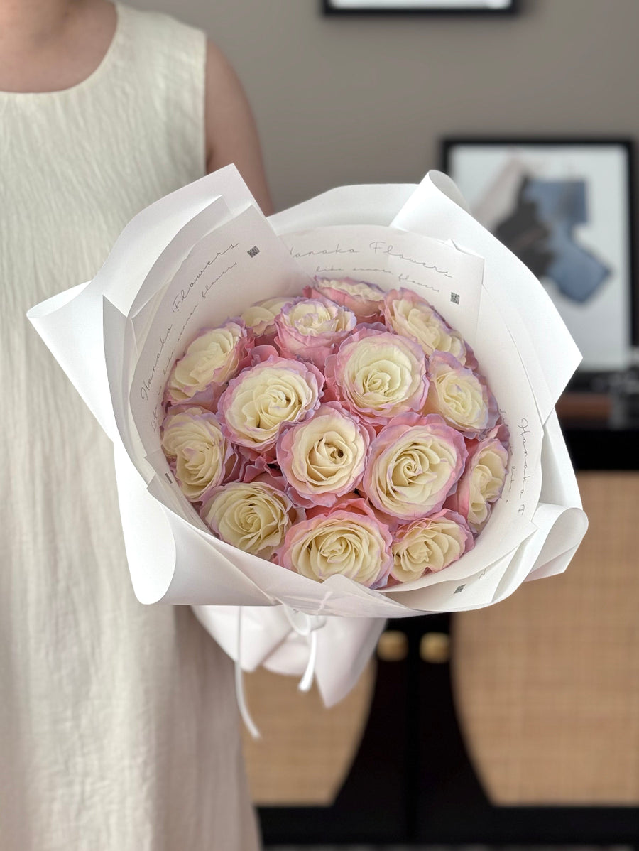Bouquet of pink and white roses wrapped in white paper held by a person.
