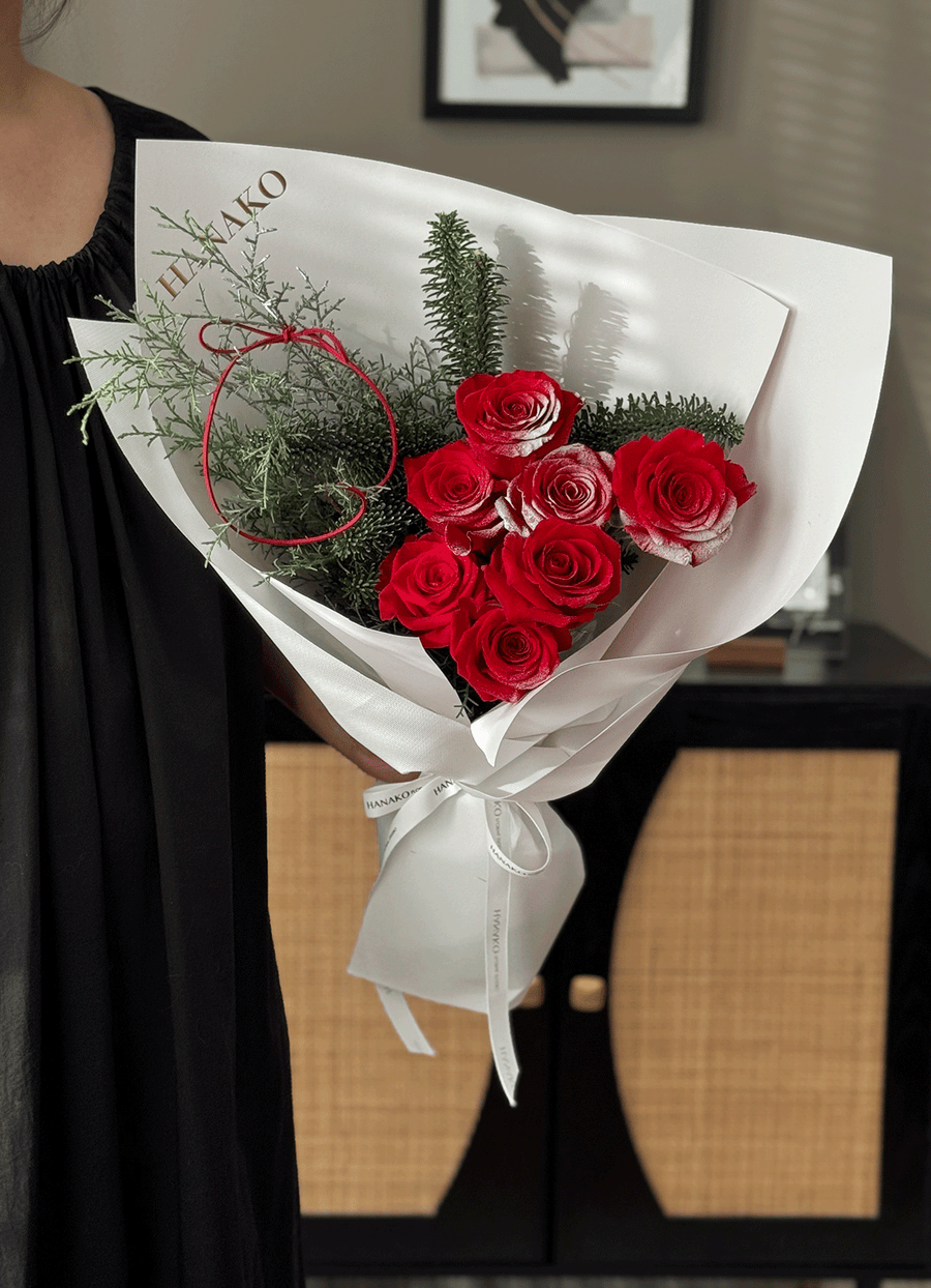 Bouquet of red roses with greenery wrapped in white paper held by a person.