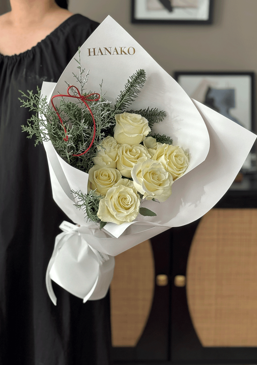 Bouquet of white roses with greenery and a red ribbon, branded 'HANAKO', held by a person.