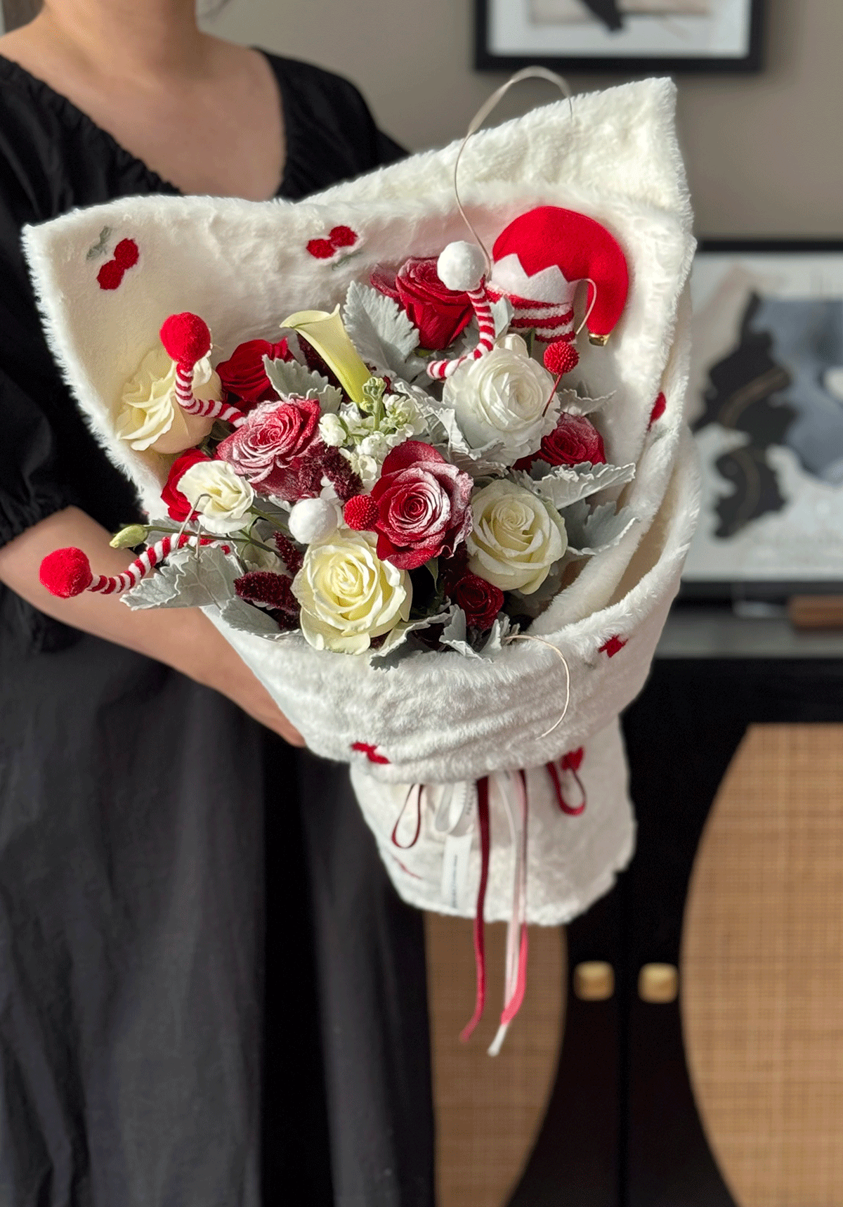 Bouquet of red, white, and gray flowers wrapped in white paper held by a person.