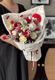 Bouquet of red, white, and gray flowers wrapped in white paper held by a person.