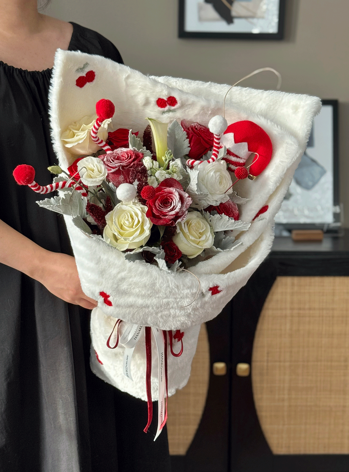 Bouquet of red and white flowers wrapped in white paper with decorative elements, held by a person.