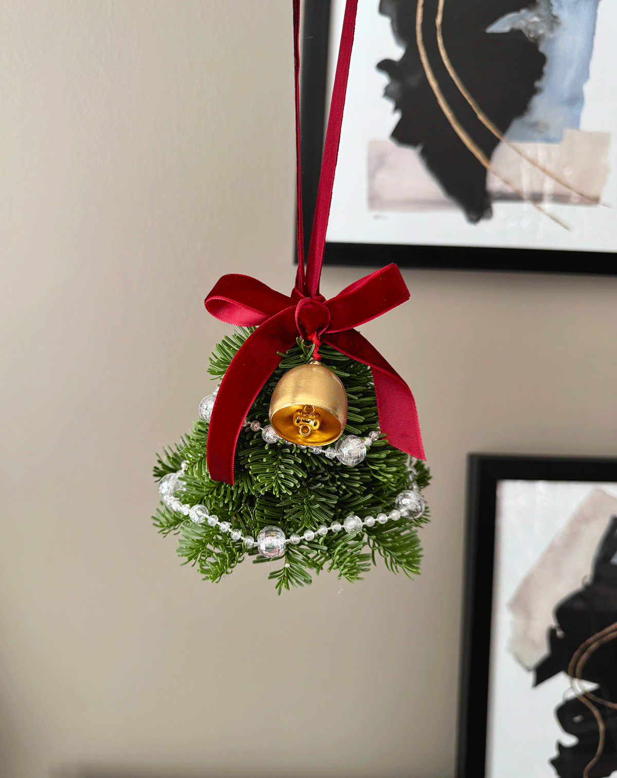 Decorative Christmas ornament with a gold bell, red ribbon, and greenery on a neutral background.