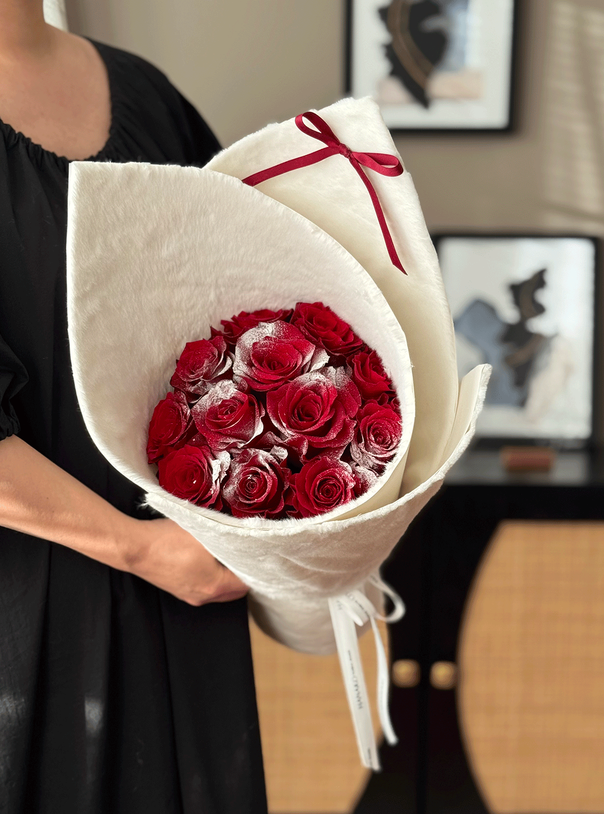 Bouquet of red roses wrapped in white paper with a red ribbon, held by a person in a black dress.