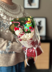 Bouquet with decorative items including a small tree and candy cane-shaped ornaments, held by a person wearing a patterned sweater.